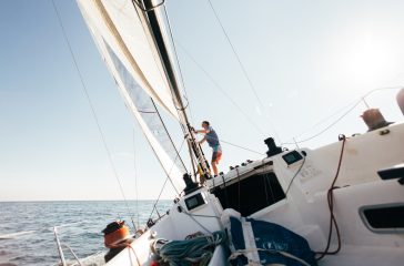 Deck of professional sailboat or racing yacht during competition on sunny and windy summer day, moving fast through waves and water, with spinnaker up, and ropes tied around winch